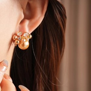 Close-up of gold flower earrings with pearls and zircons worn on the earlobe