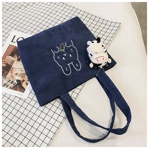 Detail view of blue corduroy tote bag with rabbit embroidery and plush cow charm