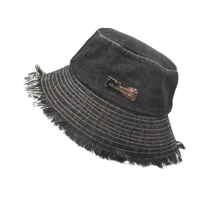 Detail of frayed edges and stitching on a black washed denim bucket hat with metal logo