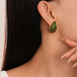 Détail de boucles d'oreilles vintage dorées avec émail vert et pierre précieuse sur modèle