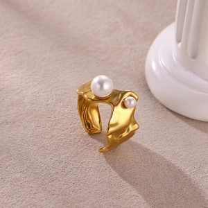 Gold irregular wrinkled metal ring with two pearls on a white decorative pedestal