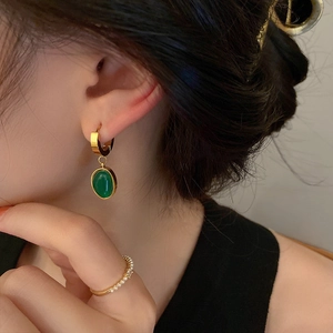 Elegant gold titanium earrings with green oval stones and a pearl ring shown on model
