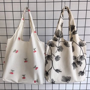 Detail of canvas tote bags featuring red cherry and black plant floral embroidery