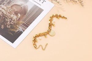 Detail of gold double-layer chain bracelet with pearl charms and a hand emblem coin