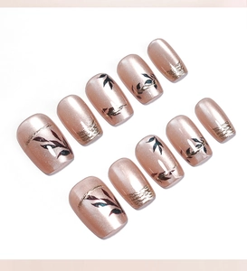 Detail of rose gold cat eye press-on nails with leaf patterns and gold foil flakes
