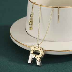 Detail of two-tone gold and silver letter R pendant necklace with lobster clasp and chain