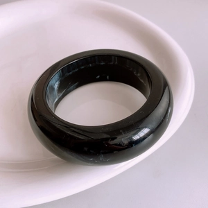 Macro detail of wide black resin bangle with white marble texture on a white ceramic plate