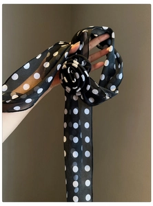 Detail view of a black chiffon scarf necklace with white polka dots and flower shape