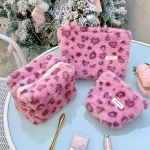 Detailed set of three pink heart leopard faux fur cosmetic bags on a white table