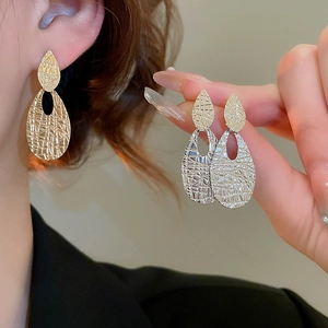 Detailed view of oval textured pendant earrings in polished gold and silver finishes