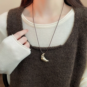 Detail of a golden croissant pendant on a dark brown cord worn over a knit vest