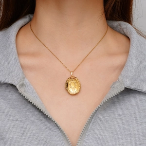 Elegante collana con medaglione ovale dorato e incisione vintage, indossata da una modella