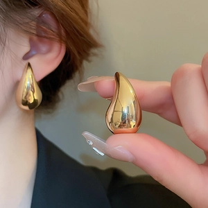 Detailed view of teardrop earrings in gold-tone metal worn by a model for size and shine