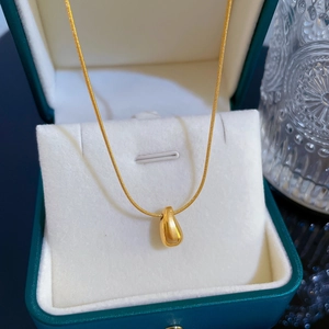 Macro shot of gold water drop pendant on a snake chain inside a dark green jewelry box