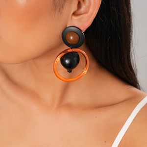 Détail de boucles d'oreilles géométriques avec disque noir mat et perle en bois sur modèle