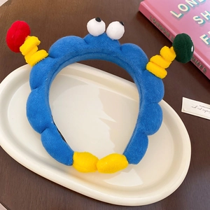 Detail eines blauen Plüsch-Cartoon-Stirnbands mit 3D-Augen und bunten Akzenten