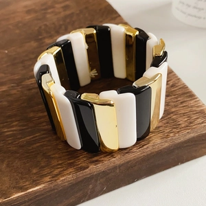 Close-up of a wide elastic bracelet with black white and gold geometric blocks on wood