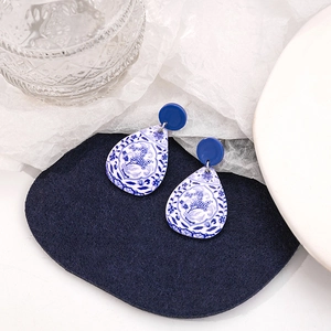 Detail view of blue and white porcelain style drop earrings on a navy felt background
