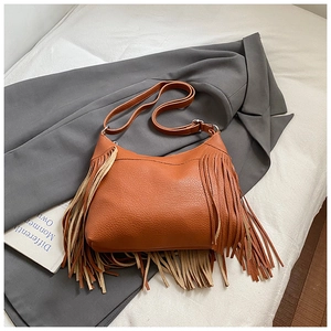 Close-up of brown leather shoulder bag with tassels on a grey suit and white sheet
