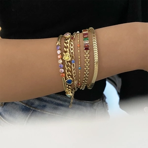 Détail de bracelets superposés en acier doré avec zircons multicolores sur le poignet