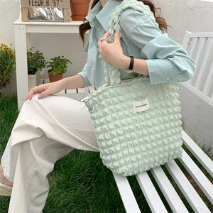 Detail of light green bubble texture tote bag with a wide shoulder strap in outdoor setting