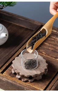 Close-up of loose leaf black tea being poured into a glass jar with a bamboo spoon