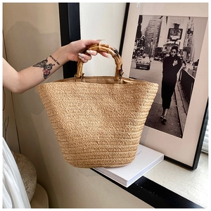 Detail of khaki straw tote bag featuring round bamboo handles and natural woven texture