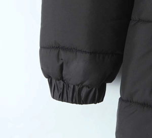 Dettaglio dei polsini elastici a coste e della trama trapuntata di un piumino nero donna