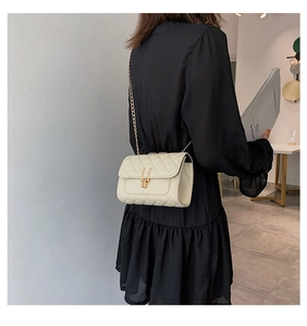 Detailed view of beige quilted chain bag with gold lock worn by model on shoulder