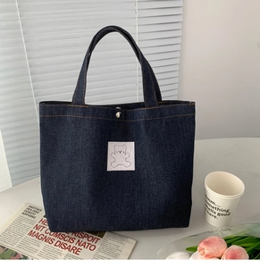 Detail of dark blue denim tote bag with white bear embroidery on marble surface