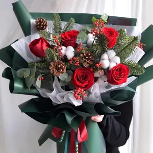 Christmas bouquet with red roses, pine cones and cotton in festive green packaging