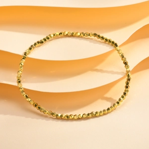 Close-up of golden faceted bead bracelet on minimalist cream wavy paper background
