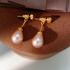 Close-up of elegant gold drop earrings with pink pear-shaped pearls on velvet