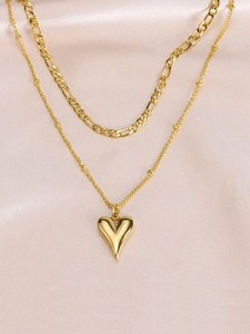 Dettaglio di una collana dorata a due strati con ciondolo a cuore su seta rosa
