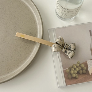 Detail shot of a beige hair clip with a marble pattern bow on a ceramic plate