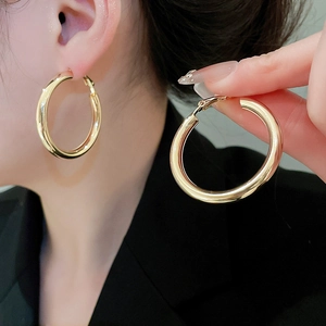 Close-up of polished large gold hoop earring with reflective metallic finish worn by model