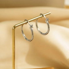 Close-up of minimalist silver hoop earrings on a display stand with silk background
