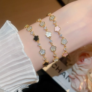 Detailed view of three gold clover charms bracelets with enamel and zircon on wrist