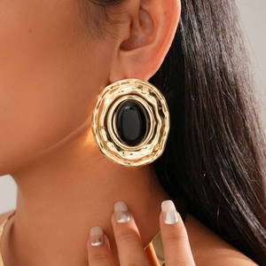 Detailed view of large retro gold hammered earrings with oval black stone on female model