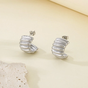 Macro shot of silver ribbed C-shape earrings on a textured stone over cream background