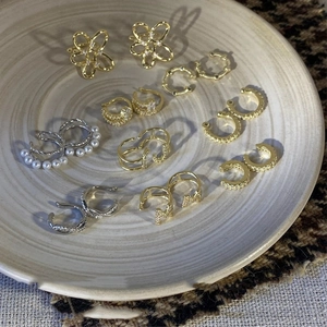 Elegant gold and silver plated bow earrings with pearls and zircons on a ceramic plate