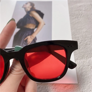 Close-up of black thick square sunglasses with transparent red lenses and metal details