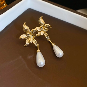 Close-up of gold-plated flower drop earrings with elegant teardrop pearls on a tray