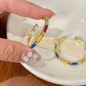 Detail of colorful enamel C-shape hoop earrings with crystals held by a hand
