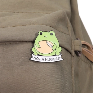 Detailed view of an enamel frog pin with Not A Hugger banner on a canvas backpack