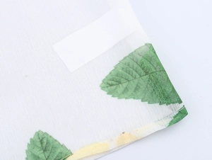 Détail d'un tissu en maille blanche avec imprimé de feuilles vertes et texture transparente