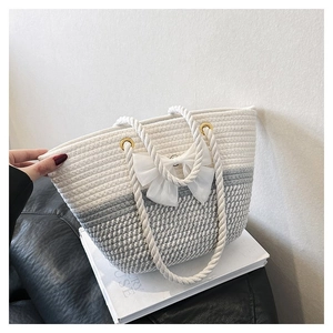 Detail of hand-woven tote bag with white bow and rope handles on a black sofa