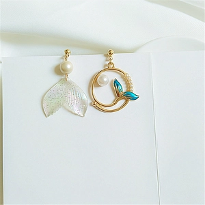 Detailed macro view of asymmetric mermaid earrings with blue whale tail and white pearl