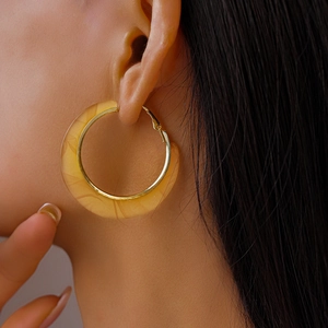 Close-up of C-shaped resin hoop earrings with yellow marble pattern and gold metal inner lining