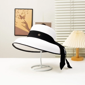Detail of white straw sun hat featuring black ribbon and gold M letter metal emblem